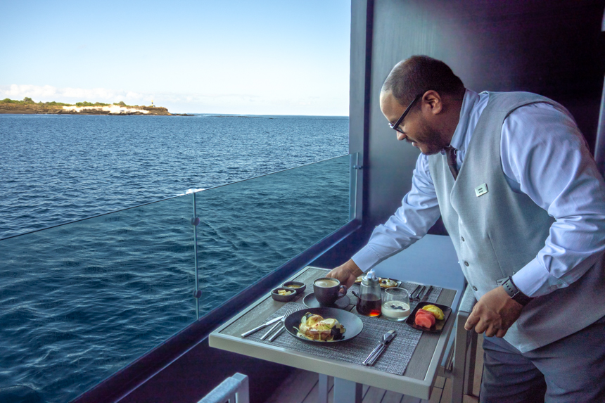 A butler places a latte on a table on the balcony of Hermes catamaran