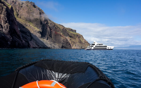 Hermes Galapagos catamaran seen from a Zodiac view with the rocky cliffs of Isabela Island behind it.
