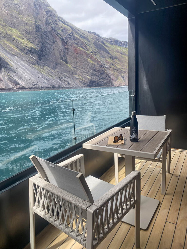 The balcony of Hermes Double Suite showing two chairs, a table and the clear glass railings looking out to Isabela Island cliffs